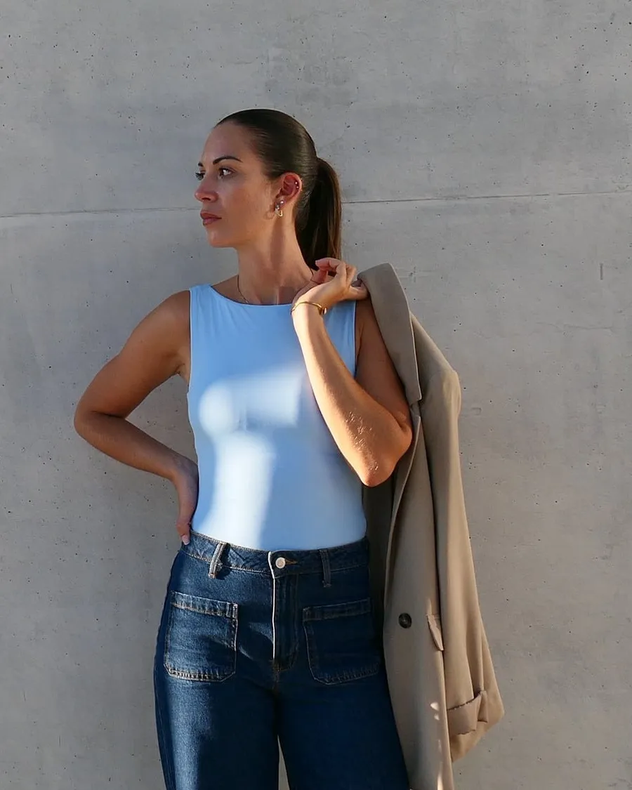 Fenella Rauscher devant un mur de béton, une veste beige sur l’épaule